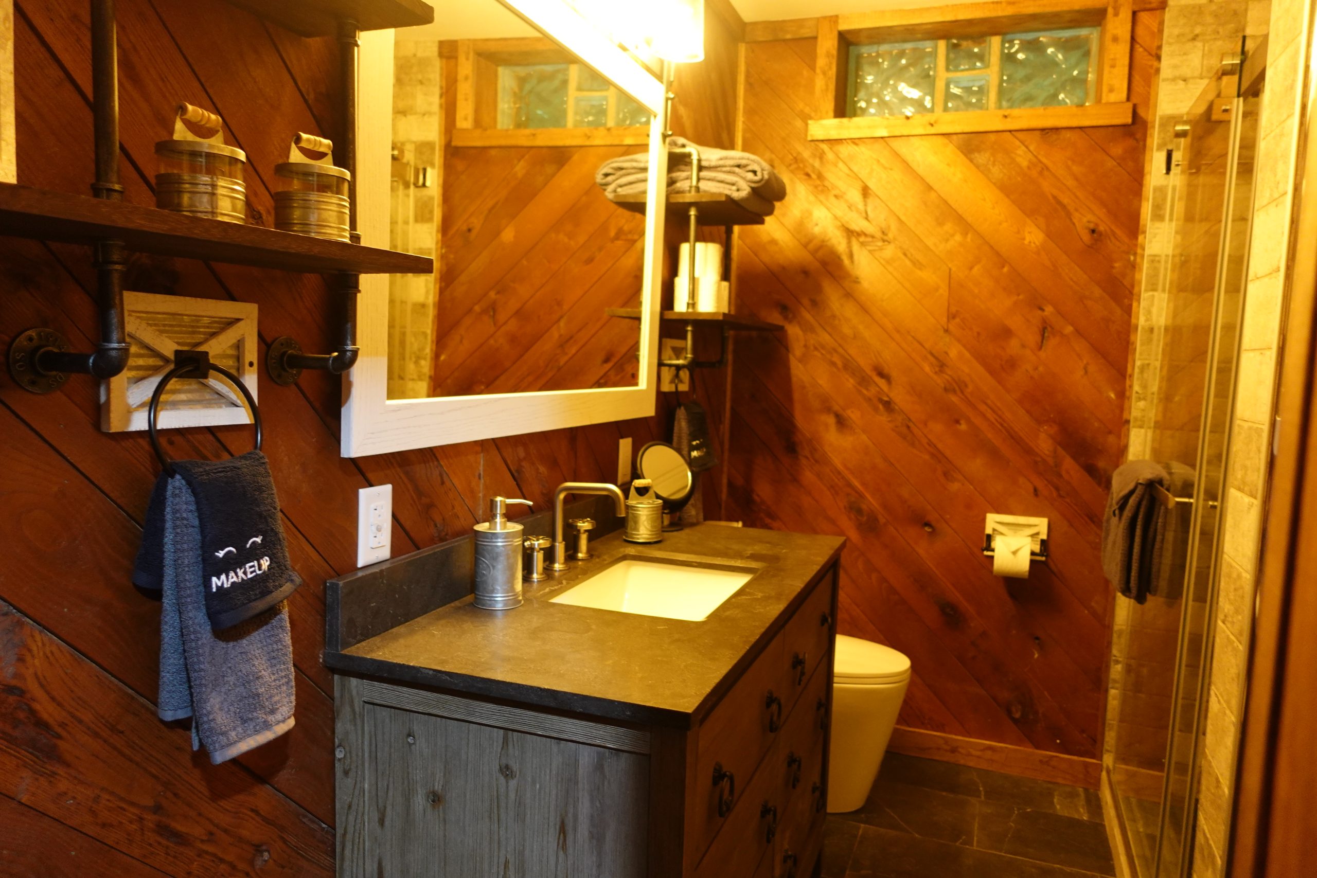 the first full bathroom, featuring a vanity with large lit mirror and a full shower, as well as a toilet